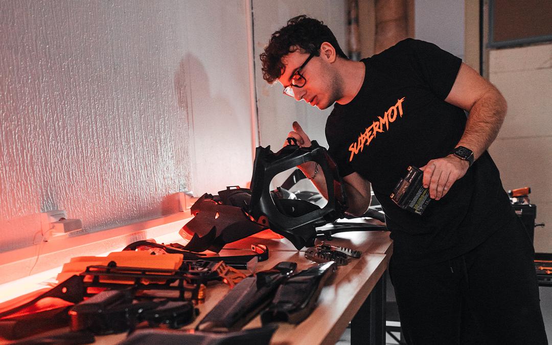 Valentin en t-shirt SUPERMOT, penché sur l'établi